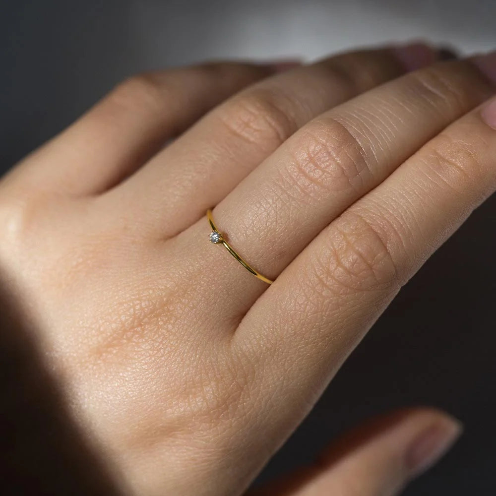 Close up of a hand wearing a gold ring with a small diamond on a dark background